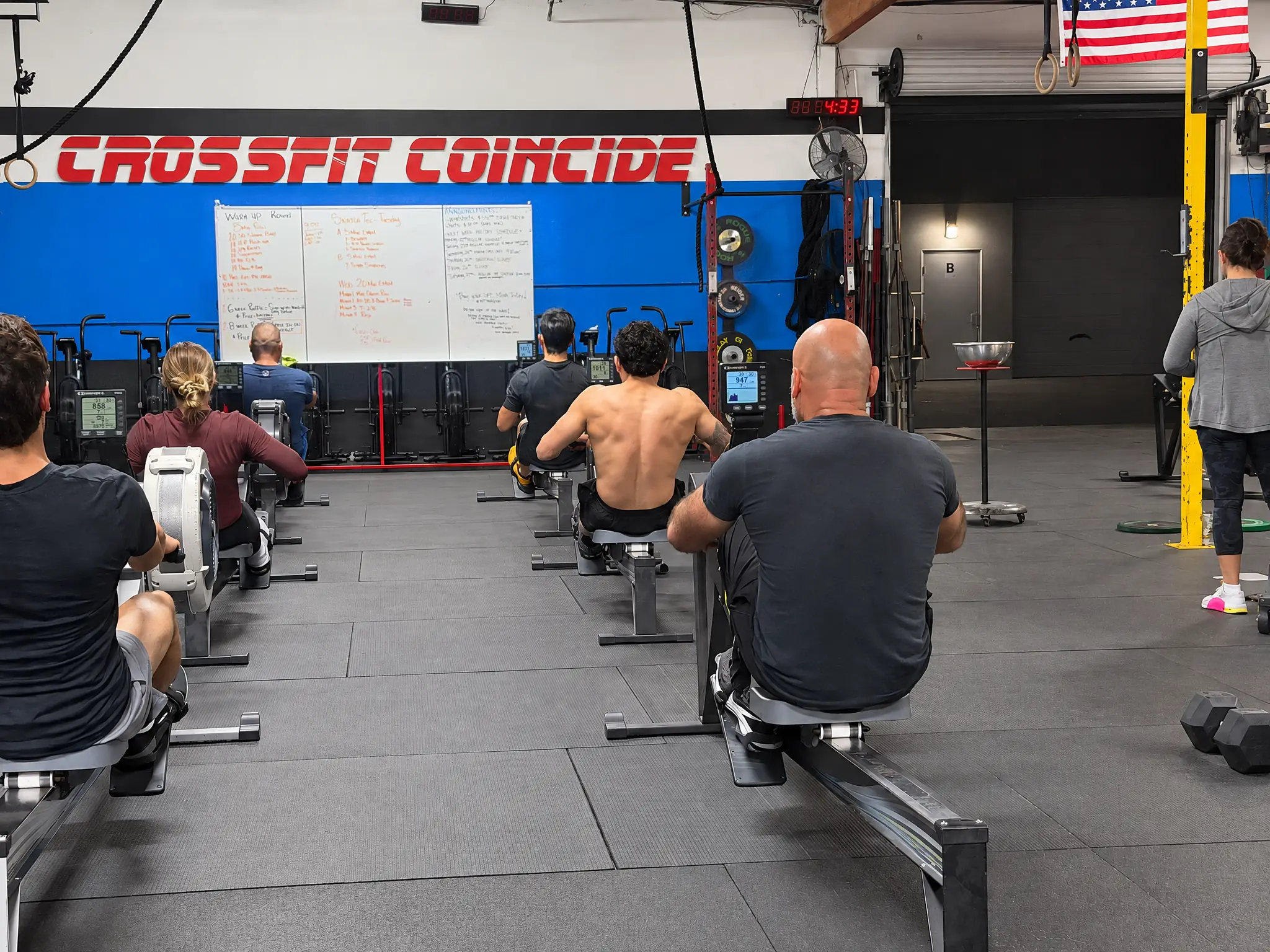 A class on the rowing machines in front of the CrossFit Coincide sign