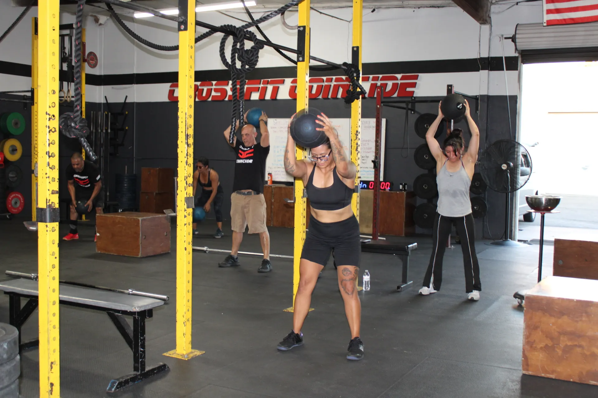 A class at Coincide lifting slam balls overhead in front of the CrossFit Coincide sign