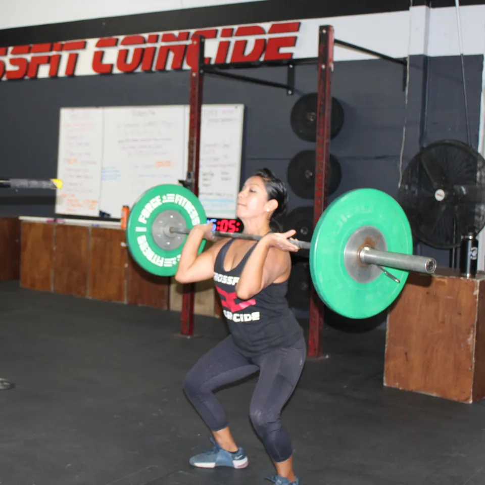 A member holding a barbell at her shoulders