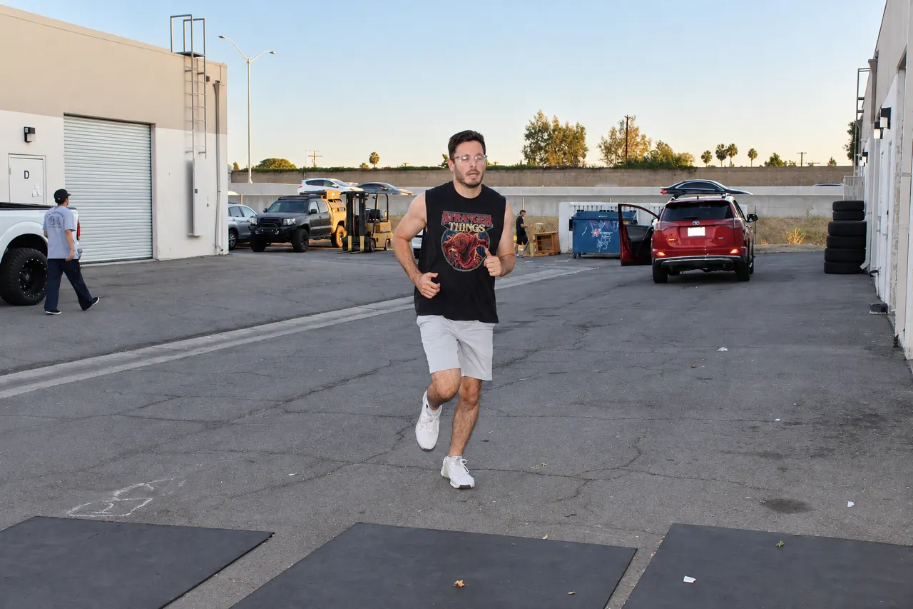 A member running in the lot outside the gym, the wall of the 22 freeway behind him